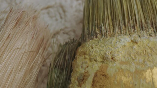 Panning macro close up of several used brushes and paintbrushes on table with a wool cover.