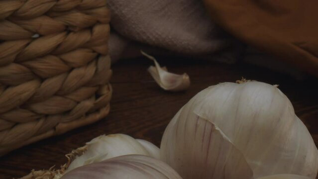 Dolly out macro close up view of various raw unpeeled garlic heads on wooden table
