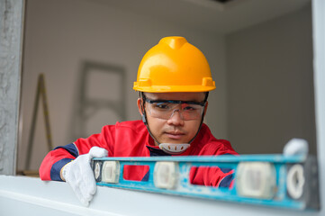 Asian male construction worker using spirit level to measure the level of construction work, spirit level used in interior decoration On the bare concrete wall of a house at a construction site