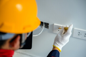 An electrician is testing electrical power and installing electrical switches in homes and building panel breakers.