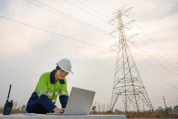 A picture of an Asian female electrical engineer using a laptop computer to stand at the electricity station to see the electric power production plan at high voltage electrode.