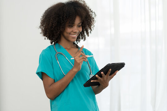 Young female doctor wearing blue scrubs uniform and stethoscope and standing holding digital tablet in hospital. African American young nurse standing working with tablet on white background