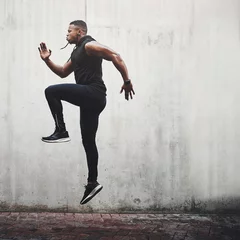 Fotobehang Jump, fitness and black man running, speed and energy for cardio training, workout and sports wellness or body health. Athlete, runner or person exercise on concrete wall, action run or moving in air © A. Frank/peopleimages.com
