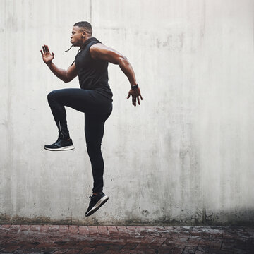 Jump, fitness and black man running, speed and energy for cardio training, workout and sports wellness or body health. Athlete, runner or person exercise on concrete wall, action run or moving in air
