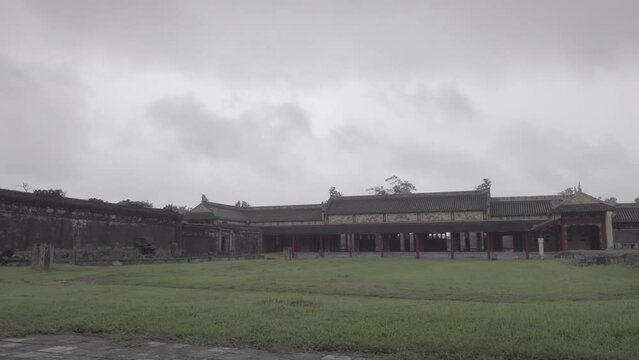 Fixed view of the Imperial City with the Purple Forbidden City within the Citadel in Hue, Vietnam on a cloudy day while clouds passing by and a small tree in the foreground LOG