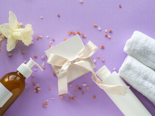 Daffodils flower, towels, sea salt, bottles and gift box with copy space on lilac background. Women and Mothers Day gift. Cosmetics and beauty care in spa salon. Hygiene, spa and relaxation as a gift.