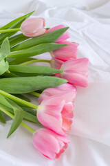 Pink tulips bouquet lying on white wrinkled blanket background copy space