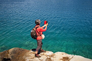 Fototapeta na wymiar Senior woman standing at the lake shore and taking photo