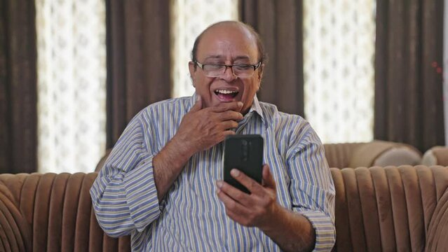 Indian old man laughing after seeing a funny thing in mobile phone