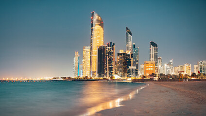 Stunning sandy beach near Corniche seaside embankment with great night view of Abu Dhabi, UAE towering skyscrapers