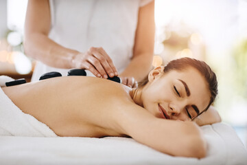 Fototapeta na wymiar Relax, hot stone and woman getting a back massage at a spa for luxury, calm and natural self care. Beauty, body care and tranquil female person sleeping while doing a rock body treatment at a salon.