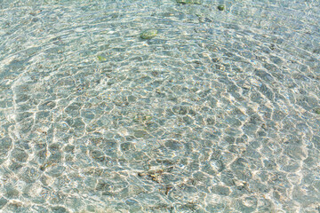 Sea water round waves texture, ripples water surface, concentric rings  of falling drops, transparent light blue ocean water top view, clear aqua background, sun glow reflection, tropical island beach