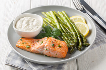 Delicious baked salmon with crispy asparagus served with tartar sauce close-up in a plate on the...