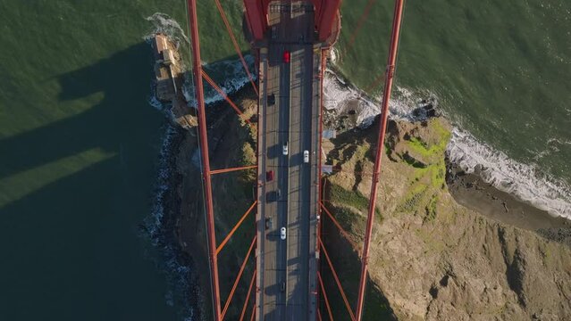 Top down view of traffic on Golden Gate Bridge in late afternoon sunshine. Fly over tower of large suspension bridge. San Francisco, California, USA
