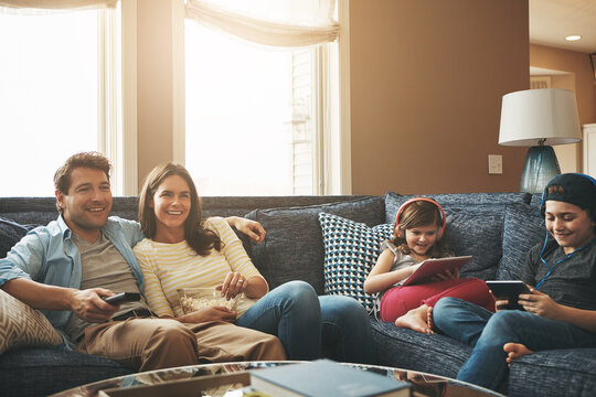 Technology, happy family together and in living room of their home with lens flare. Connectivity, networking or streaming and parents watching tv with children on tablet or smartphone with headphones