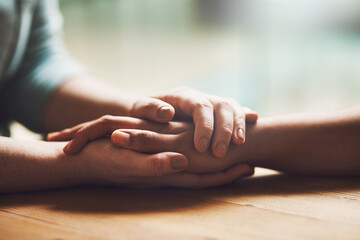 Love, empathy and support with people holding hands in comfort, care or understanding on a wooden table of a home. Prayer, faith or depression with friends closeup for hep, hope or peace for healing - obrazy, fototapety, plakaty