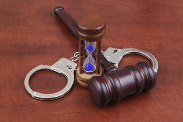 Wooden judge gavel with handcuffs and hourglass. Court and time concept.