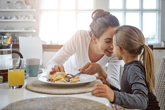 Mother, child and pancakes for breakfast in a family home with love, care and happiness at a table. A happy woman and girl kid eating food in plate together in morning for health and wellness