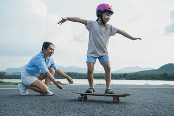 Mother teaching her daughter how to skateboard in the park. Child riding skate board. Healthy...