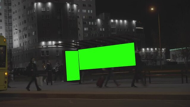 Citylights with green chromakey installed at transport stop against illuminated building and street traffic. City life at night time lapse