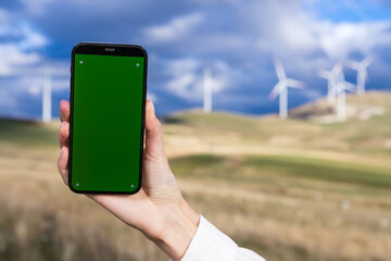 Close-up of a smartphone with a chromakey in the hand of an engineer against the background of wind turbines. Wind power plant, power generation