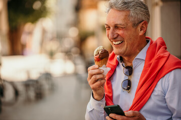 Smart casual dressed businessman eating ice cream and using a phone in the city.