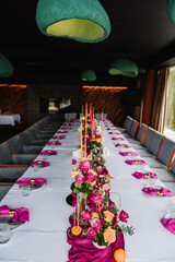 Luxury elegant table setting dinner with floral centerpiece in a restaurant. Decoration with pink and orange flowers roses, candles, fruits. Plate, dishes, glasses, forks, napkins. Decor rustic style.