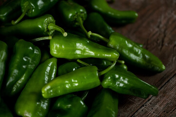 Green hot Padron pepper. Lot of ripe peppers on wooden surface. Pepper harvest. Pepper cultivation. Bright spices. Spicy food. Spanish pepper. Wooden background. Close-up. Soft focus. Top view. 