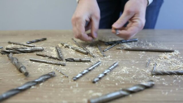  Drills for drills of different diameters lie on the table. A man chooses drills for drilling.