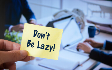 Male hand holding sticky note written Don't Be Lazy.