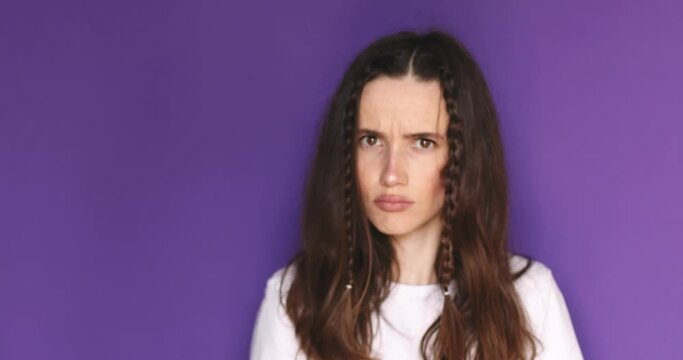 Angry furious brunette woman with two braids shaking fist at camera, purple studio background. Protest, angry feministic woman look at camera.