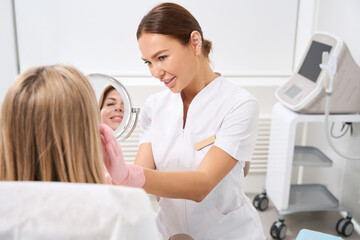 Cosmetologist in clinic of aesthetic medicine consults patient in bathrobe
