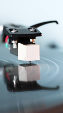 Needle of Vintage DJ Turntable Spinning Vinyl Record on light blue background