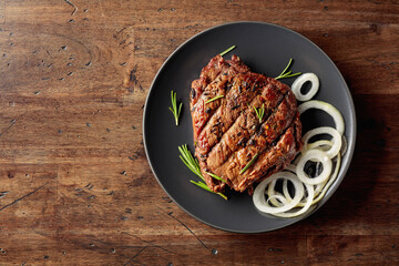Grilled ribeye beef steak with rosemary and marinated onion on a black plate.