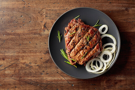Grilled ribeye beef steak with rosemary and marinated onion on a black plate.