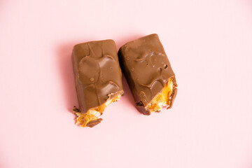 Pieces of delicious chocolate bar with nougat, caramel and peanuts on a pink background