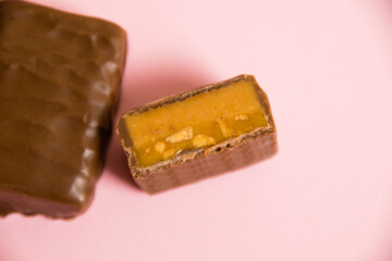 Flatlay, sweet chocolate bar with salted caramel macro on pink paper background with copy space