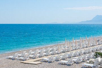 Landscape coast with white beach umbrellas and sun loungers on the sand beach, against the backdrop...