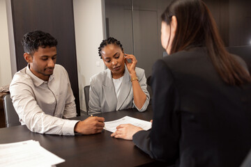 Shot of an insurance agent with a multi-ethnic couple looking through documents in the office.