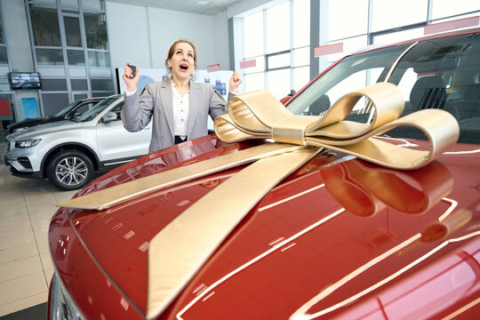 Happy woman standing near car with golden bow on hood