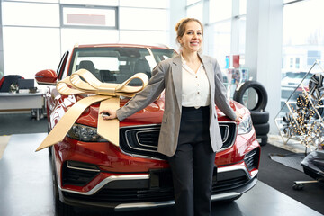 Happy lady standing in front of red automobile in cardealership