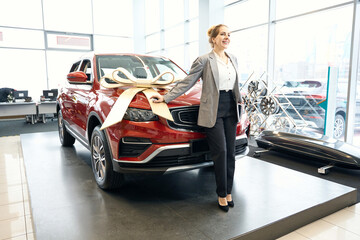 Happy lady standing in front of red automobile in cardealership