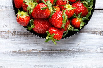 Organic strawberries in a black plate on a light wooden background, top view, copy space
