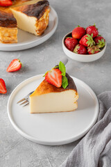A piece of Basque burnt cheesecake or San Sebastian cheesecake with fresh strawberries on a white plate on a gray background. Selective focus. Copy space.