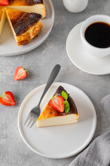 Fototapeta premium A piece of Basque burnt cheesecake or San Sebastian cheesecake with fresh strawberries on a white plate on a gray background. Selective focus. Copy space.