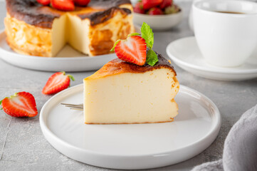 A piece of Basque burnt cheesecake or San Sebastian cheesecake with fresh strawberries on a white plate on a gray background. Selective focus. Copy space.