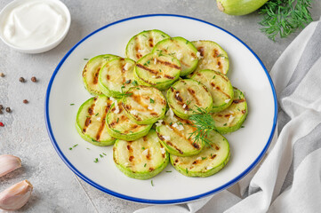 Slices of fried zucchini with garlic and fresh dill on a plate on a gray concrete background. Vegetarian healthy dish. Selective focus.