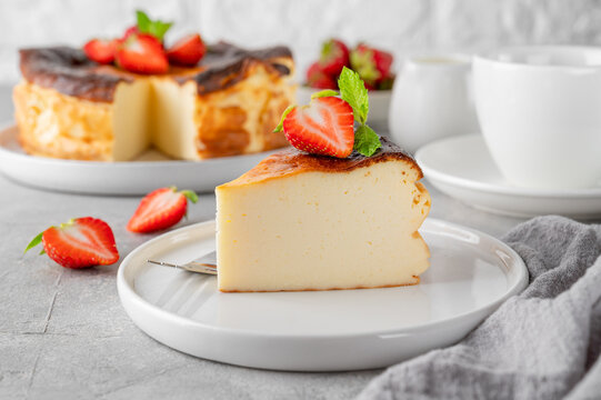 A piece of Basque burnt cheesecake or San Sebastian cheesecake with fresh strawberries on a white plate on a gray background. Selective focus. Copy space.