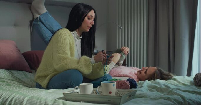 Portrait of Two Young Female Friends Knitting Together While Hanging Out in the Bedroom. Girls Chatting and Laughing While Relaxing and Practicing Their Favorite Hobby Together