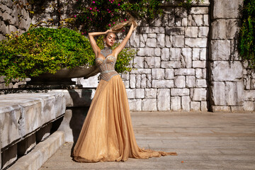 Elegant luxury evening fashion. Glamour, stylish elegant woman in long gown dress is posing in luxury hotel outdoor. Female model in amazing long dress. Outdoor shoot. Vogue. Couture.